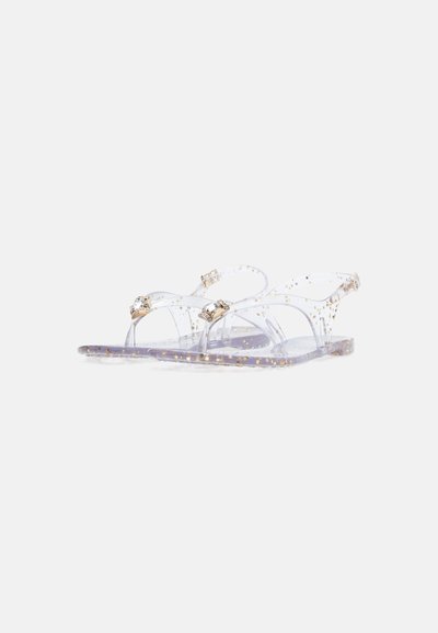 Sandales transparentes avec un motif de points dorés scintillants, semelle plate et brides décoratives ornées d'une touche de strass.
