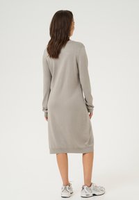 Robe en tricot longue et ajustée de couleur gris clair, fabriquée dans un tissu doux avec des manches longues et un col rond ; longueur genoux avec des accents côtelés au niveau de l'ourlet.