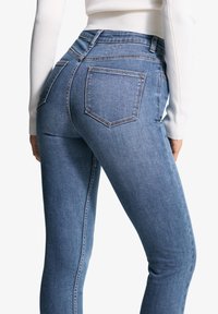 Siniset farkut, joissa on kapea malli, korkea vyötärö, viisi-taskinen muotoilu ja näkyvät saumat. Tasainen tekstuuri ja suora lahkeensuun leikkaus.