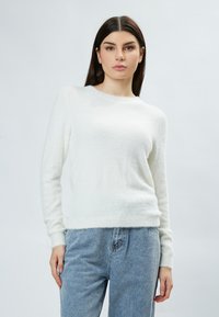 Maglione bianco peloso con maniche lunghe e scollatura rotonda, abbinato a jeans azzurri chiari. Tessuto morbido e vestibilità rilassata.