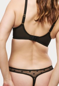Zwarte mesh beha met dunne bandjes en een haaksluiting, gecombineerd met een bijpassende sheer string versierd met kleine zwarte bloemenpatronen.