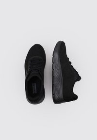 Czarne buty sportowe z przewiewną siateczkową cholewką, teksturowaną podeszwą, wyściełanym kołnierzem i płaskimi sznurowadłami. Brak widocznych oznakowań na zewnętrznej stronie.