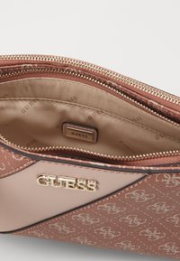 Worek z zamkiem błyskawicznym w różowawym syntetycznym materiale, posiadający wzorzystą zewnętrzną stronę oraz złote akcesoria z markową metką wewnątrz. Teksturowane wykończenie.