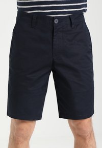 Mörkblå bomullsshorts med flat framtill, knappstängning och sidofickor. Slät struktur och rak bendesign.
