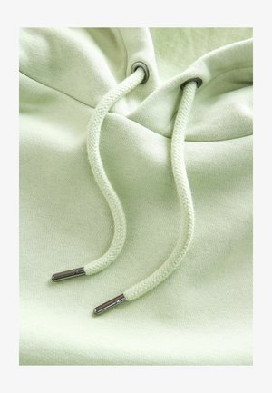 Világoszöld kapucnis pulóver, puha tapintással, fém végekkel ellátott húzókákkal és lekerekített kapucnival. Diszkrét varrási részletek láthatók.