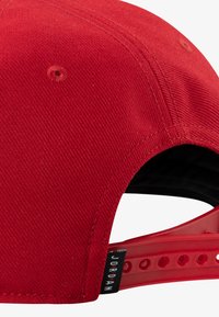 Red baseball cap featuring a textured fabric with a solid design, plastic adjustable strap, and a logo tag on the side.