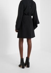 Mustat paita napituksilla selässä, yhdistettynä mustiin hameeseen. Mallilla on mustat nilkkurit, joissa on paksu korko. Sileä materiaali.