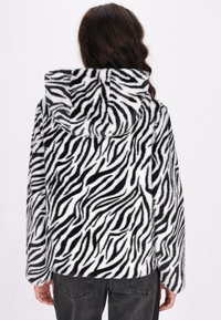Giacca in fleece a stampa zebrà in bianco e nero con cappuccio, caratterizzata da una texture morbida e maniche lunghe. Il design ha una silhouette casual.