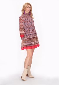 Rochie colorată, cu model floral, gât înalt, mâneci lungi, tiv în straturi și accente roșii; asortată cu cizme de cowboy bej.