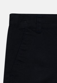 Pantalon en denim bleu foncé avec une texture lisse, doté d'un devant plat, de deux poches latérales et de coutures bleues en accent.
