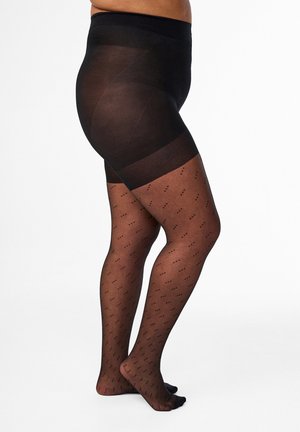 Persoon die doorschijnende zwarte panty's met patroon draagt, met verstevigde heupen en tailleband, staand met één been licht over het andere gekruist.