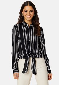 Zwart-wit gestreepte blouse met knopen en een gestrikte voorkant, gemaakt van een gladde stof. Heeft lange mouwen en een klassieke kraag.
