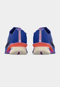 Ζευγάρι μπλε παπούτσια για τρέξιμο Nike, με θέα από πίσω, που διαθέτουν κόκκινες λεπτομέρειες, λευκές σόλες και ορατό λογότυπο Nike στα τακούνια.