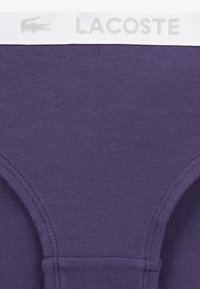 Purple cotton underwear with a smooth texture, featuring a white elastic waistband with "LACOSTE" printed in gray lettering.