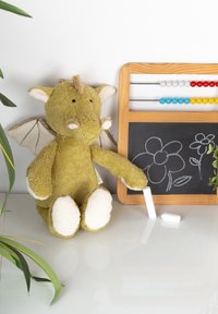 Green stuffed dragon holding chalk beside small chalkboard with flower drawings and wooden abacus on white surface.