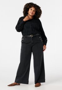 Zwarte overhemd met knopen en een gestructureerd bloemenpatroon, gecombineerd met zwart hoge taille wijde jeans met zilveren knopen en contrasterende stiksels.