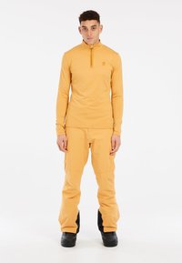 Dlhý rukáv, polovičný zips a nohavice v jasne žltej farbe, vyrobené z hladkej, pružnej tkaniny. Obsahuje jemné logo a čierne akcenty na dolnej časti.