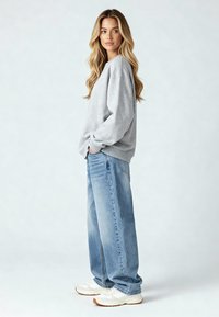 Harmaa crewneck-huppari, jossa on laskeutuvat olkapäät, yhdistettynä löysiin sinisiin farkkuihin ja valkoisiin lenkkareihin. Sujuva pinta ja rento istuvuus.