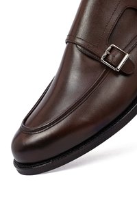 Bruine leren nette schoen met een puntige neus, decoratieve stiksels en een zilverkleurige gesp over de wreef. Gladde textuur.