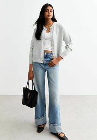 Cardigan grigio chiaro, canotta bianca aderente, jeans a gamba larga blu chiaro con orlo sfilacciato, borsa a spalla nera e scarpe nere basse con cinturini.