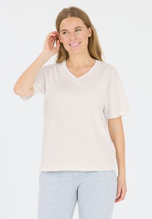 Lys beige V-hals T-shirt med korte ærmer, lavet af glat stof, parret med grå sweatpants med et lille logo nær kanten.