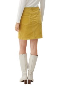 Gul kordflöjdskjol med rak skärning, bakfickor och bältesöglor, matchad med knähöga vita stövlar med klack.