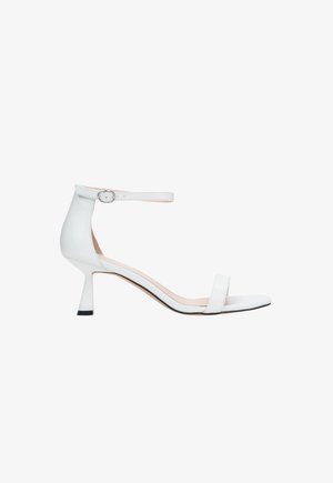 Białe skórzane sandały na obcasie z paskiem wokół kostki, otwartym noskiem, zwężanym obcasem i minimalistycznym designem. Posiadają czarny akcent na obcasie.
