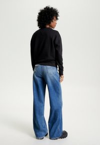 Felpa nera con polsini a coste, abbinata a jeans a gamba larga di colore blu chiaro con dettagli sbiaditi e design a due tasche posteriori. Scarpe platform nere.
