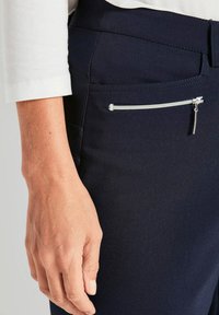 Navyblauwe broek met een strak ontwerp, een soepele textuur en een klein ritszakje aan de voorkant met zilverkleurige accenten.