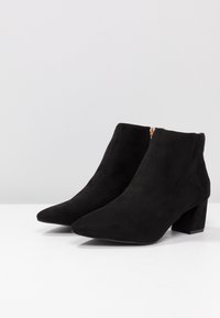 Sorte ruskinds ankelstøvler med spids tå og blokhæl. Har en sidelukning for nem adgang. Glat tekstur, minimalistisk design.
