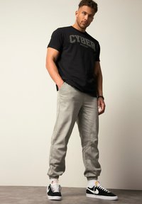 Zwarte katoenen t-shirt met "CYBER" graphic, lichtgrijze joggers met zijzakken, uitgerust met zwart-witte sneakers met veters.
