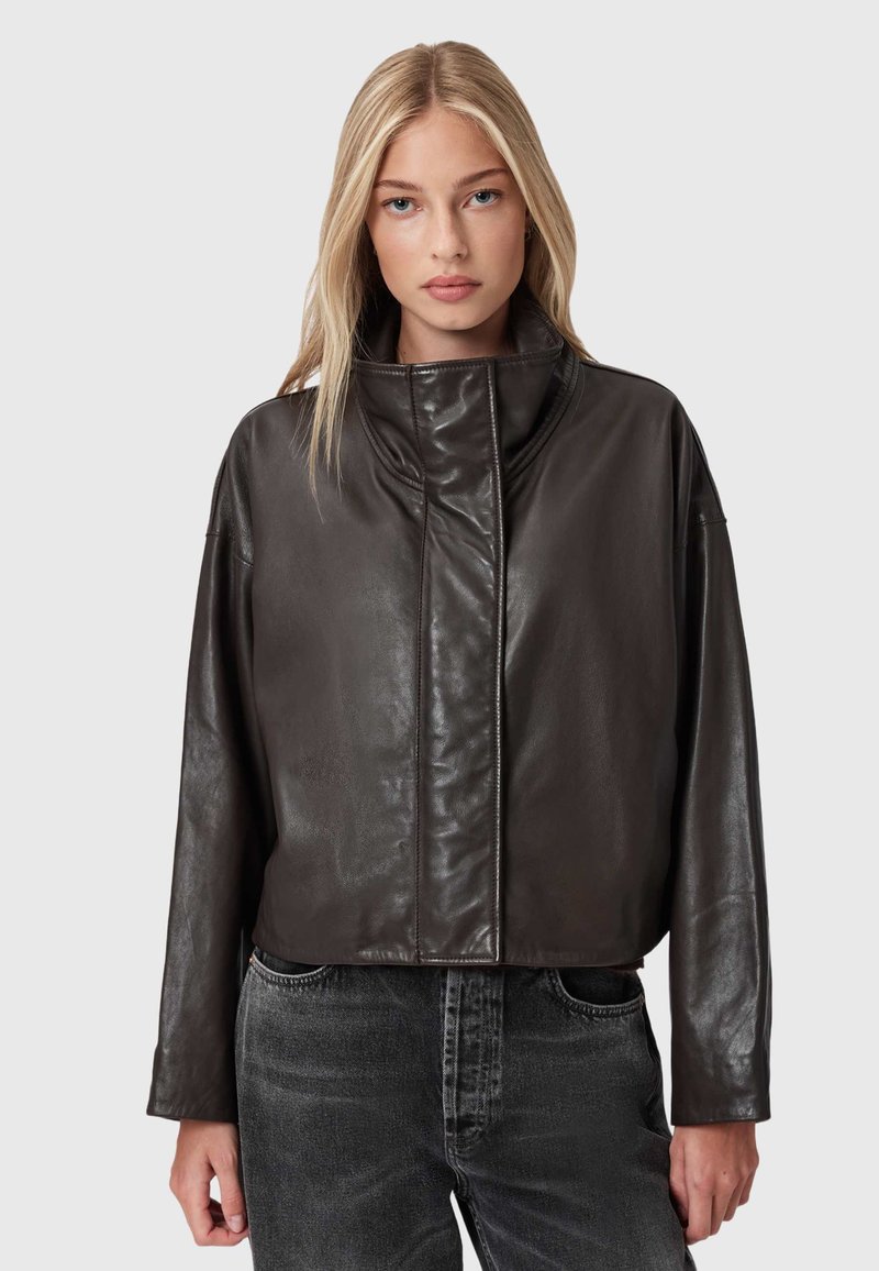 Tumši brūns ādas jaciņa ar augstu apkakli, saīsinātu dizainu un smalku spīdumu. Tam ir brīvi piedurknes un nav redzamu aizdari.