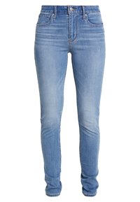 Jeans ajustados en denim azul claro; cuenta con desgastado, estilo clásico de cinco bolsillos, cierre de botón y cremallera, y detalles de costura.