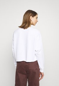 Sweatshirt branco cropped com decote redondo e mangas longas e largas. Combinado com calças de cintura alta em bordeaux com bolsos traseiros.