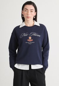 Granatowy sweatshirt z białym kołnierzykiem, z napisem "New Haven" napisanym kursywą oraz wzorem herbu, wykonany z miękkiego materiału w luźnym kroju.