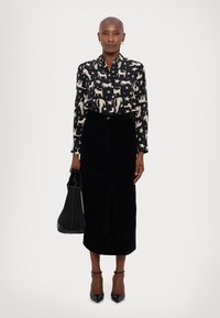Blusa nera a maniche lunghe con motivo animale e stelle, abbinata a una gonna midi in velluto nero e una borsa nera strutturata.