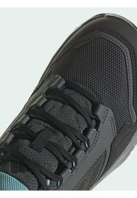 Zapatilla deportiva negra con parte superior de malla, cordones negros, acentos de goma y detalles en un verde claro, con un diseño aerodinámico y superficie texturizada.