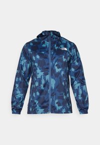 Veste coupe-vent à capuche en bleu marine et motif camouflage teal, fabriquée à partir d'un matériau léger, avec une fermeture éclair à l'avant et un logo sur la poitrine.