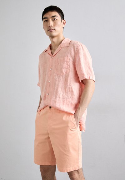 Camicia in lino rosa chiaro a maniche corte con tasca, abbinata a pantaloni corti rosa. Entrambi presentano una vestibilità comoda e una superficie liscia.
