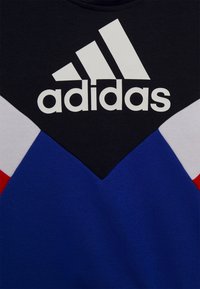 Černá, modrá, bílá a červená mikina s V-tvarovaným designem, velkým bílým logem Adidas a strukturovaným povrchem.