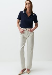 Polo shirt en maille marine avec des accents blancs au col, associé à un pantalon crème taille haute et des escarpins nude à bout pointu.