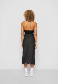 Fekete kötött crop top, nyakpánttal, amelyet egy testhezálló fekete farmer midi szoknyával párosítottak. A szoknya hátsó zsebekkel rendelkezik és egyenes vonalú.