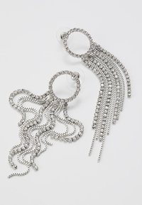 Orecchini in tono argento con design circolari decorati con strass trasparenti, dotati di catene pendenti e dettagli ondulati.