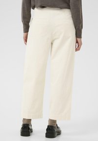 Lichtbeige corduroy broek met een wijde pijp, voorzien van twee achterzakken, gecombineerd met zwarte schoenen en grijze gebreide sokken.