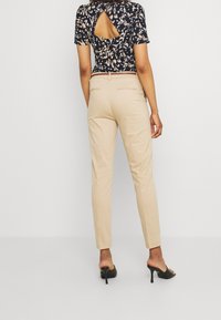 Beżowe dopasowane spodnie w połączeniu z granatową bluzką w kwiaty z wycięciem z tyłu, gładką fakturą i slim fit.