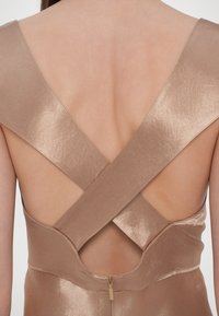 Satin kjole i en lys beige nyanse med kryssede stropper på ryggen, med glidelås i nedre del av ryggen og en glatt tekstur.