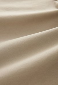 Tissu beige lisse avec une texture subtile de tissage diagonal formant de doux plis sous un éclairage doux.