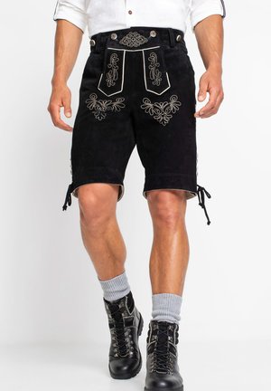 Schwarze Wildledershorts mit aufwendiger silberner Stickerei, tailliertem Bund und verstellbaren Seitenschnüren. Kombiniert mit schwarzen Schnürstiefeln und grauen Socken.