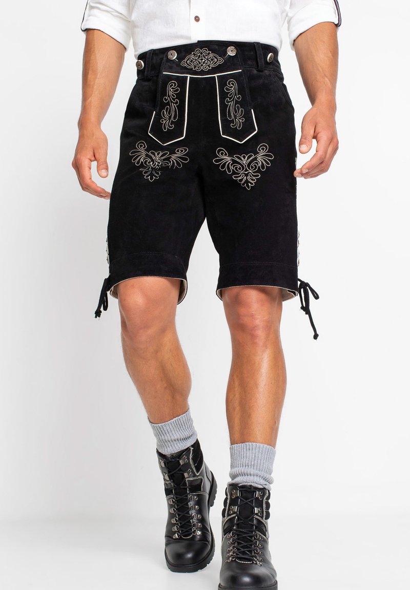 Pantaloni corti in suede neri con intricate ricami argentati, vita con cintura e lacci laterali regolabili. Abbinati a stivali neri stringati e calze grigie.