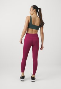 Sportslig antrekk med en mørkegrønn sports-BH og teksturerte burgunder leggings med høy midje. Kombinert med svarte løpesko.